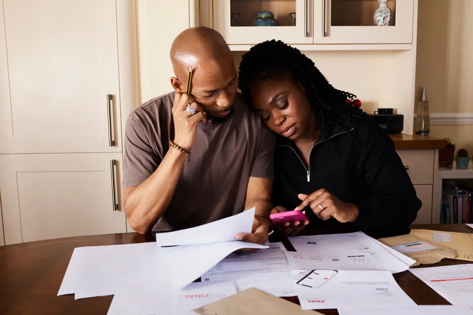 A man and a woman sitting close at a wooden table, going through bills and papers together with a phone