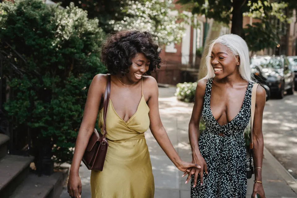 Two women laughing together as they walk hand in hand down a tree-lined street