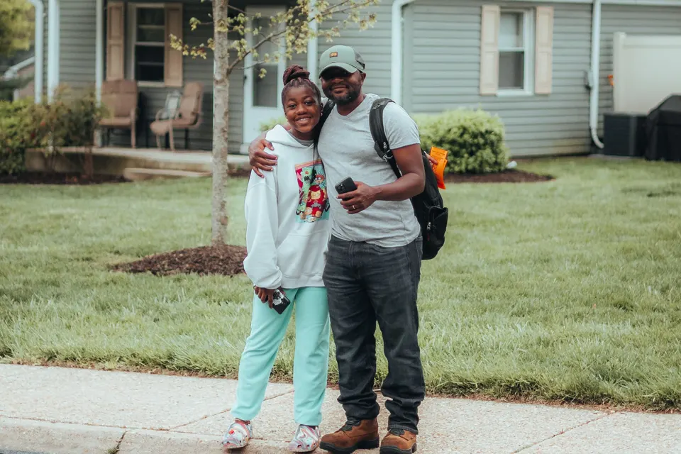 A father and his daughter standing arm in arm on the pavement in front of their home on a quiet street