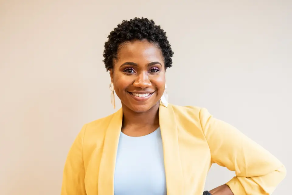 A confident woman in a yellow blazer holding a tablet and smiling at the camera