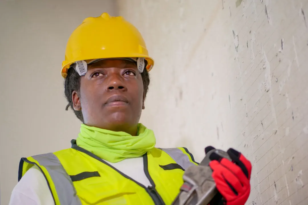 A repair technician in a hard hat and safety vest holding a pipe wrench indoors